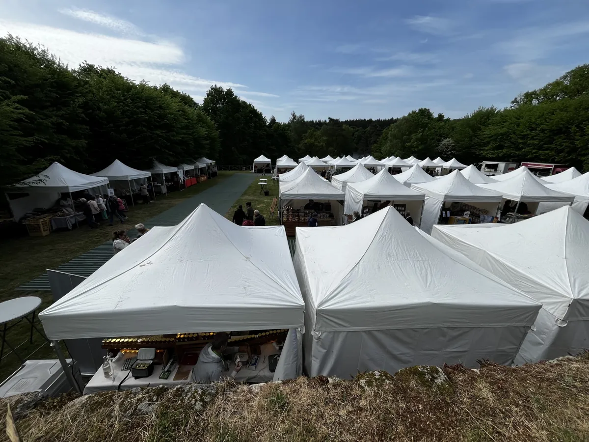 Marché en plein air sous tentes blanches, en lisière de forêt, avec allées de circulation