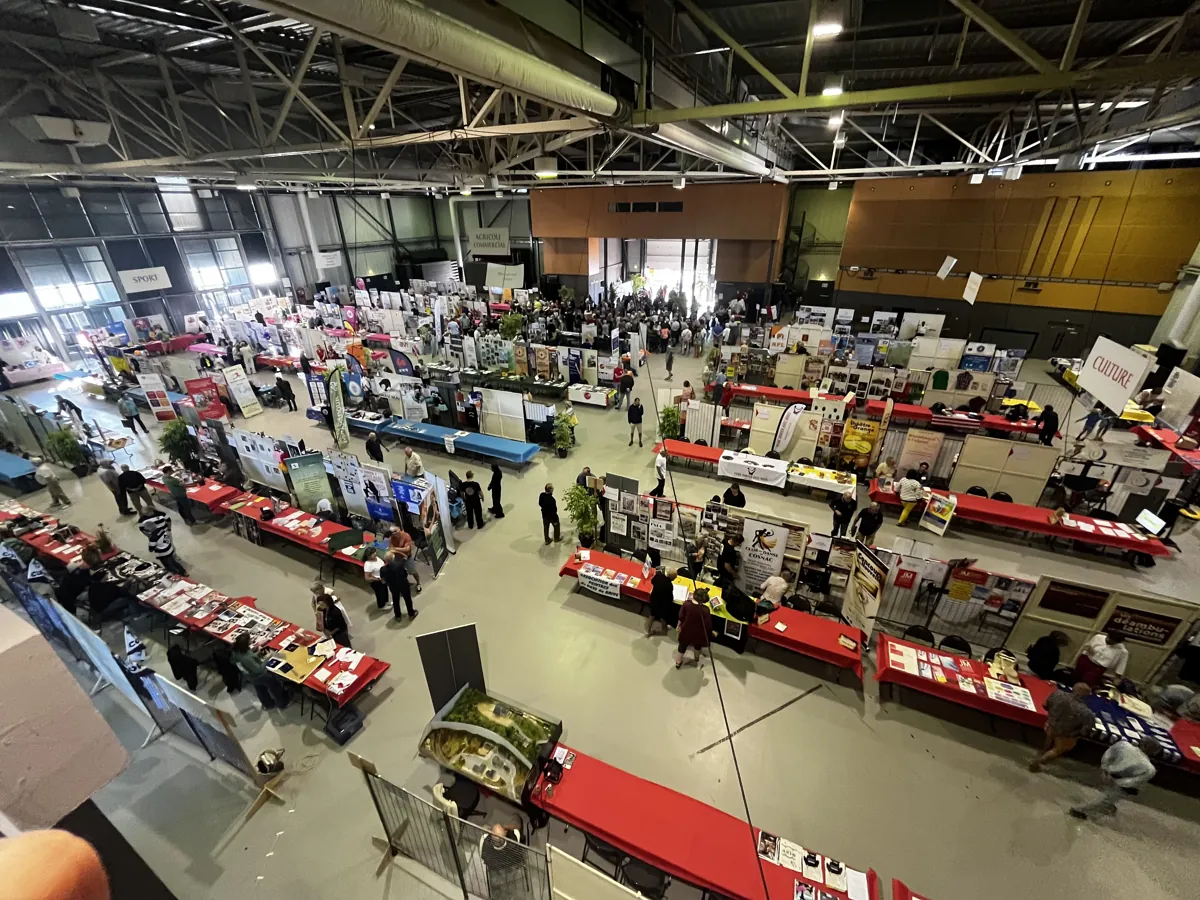 Forum des associations dans un hall d’exposition, vu depuis la mezzanine : rangées de stands et allées de circulation